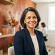 A diverse, professional individual smiling confidently in a modern, brightly lit office with warm terracotta and white decor.